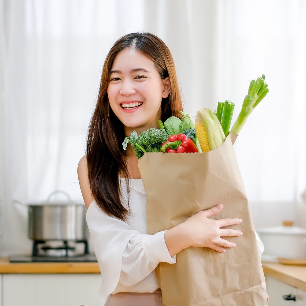 lovely girl hold bag with various vegetables and smile stand in kitchen e1649390181606.jpg